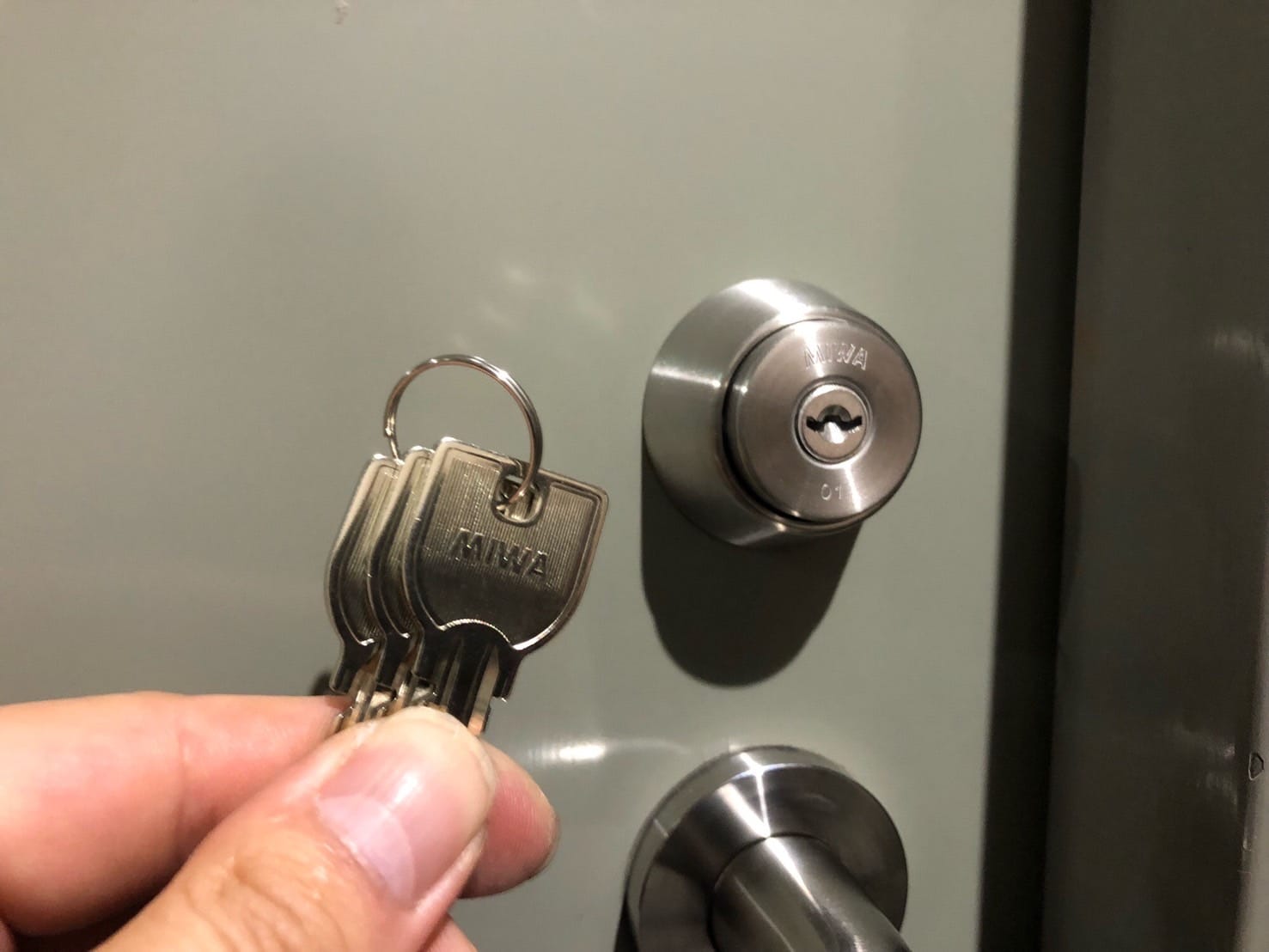 交換完了。新しいシリンダーを取り付けた扉の前で付属の鍵3本を持っている