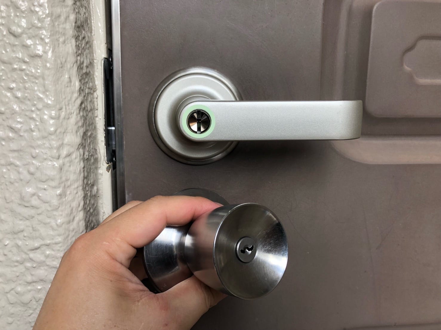 ドアに新しく取り付けたレバーハンドルの下で取り外したノブを手に持っている