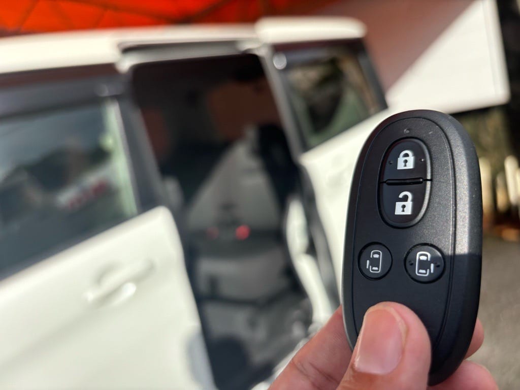 パワースライドドアが開いたデリカD2をバックにスマートキーを持っている