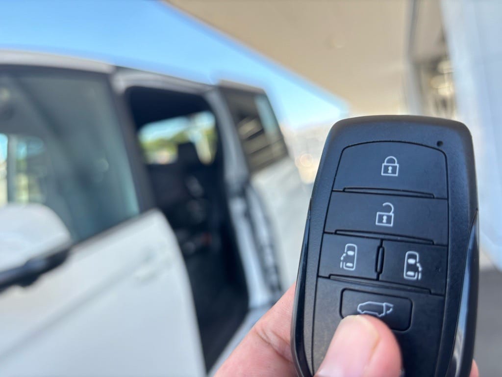 パワースライドドアが開いたヴォクシーをバックにスマートキーを持っている