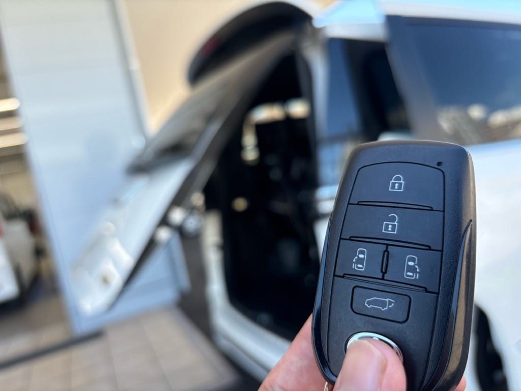 リアパワーゲートが開いたヴォクシーをバックにスマートキーを持っている