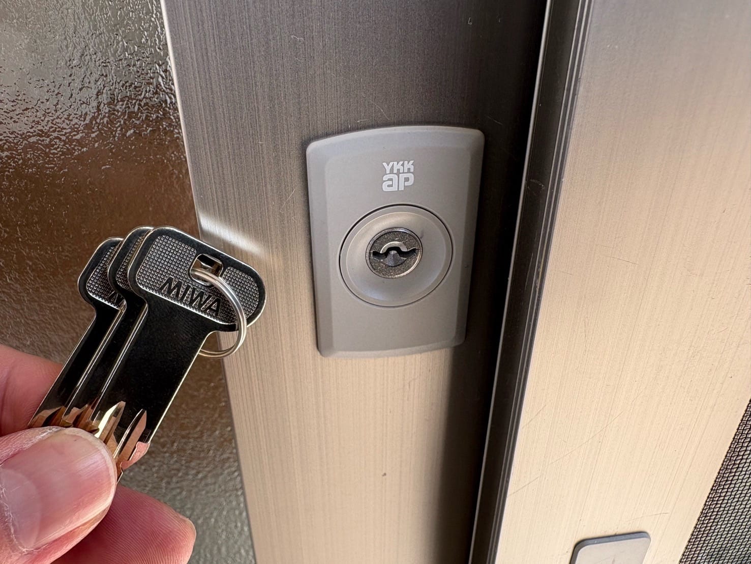 鍵交換完了。新しい鍵がついたドアの前で付属の鍵を持っている